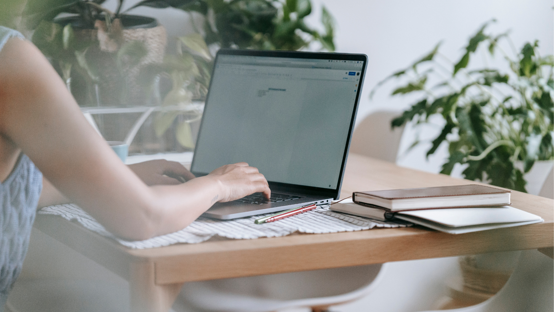 Woman working calmly on laptop at home desk with plants, notebooks and pencils