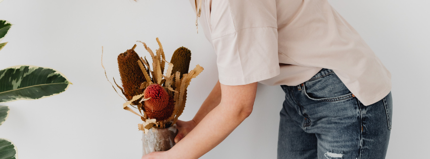 Woman arranging dried flowers in rustic vase, minimalist home decor setting