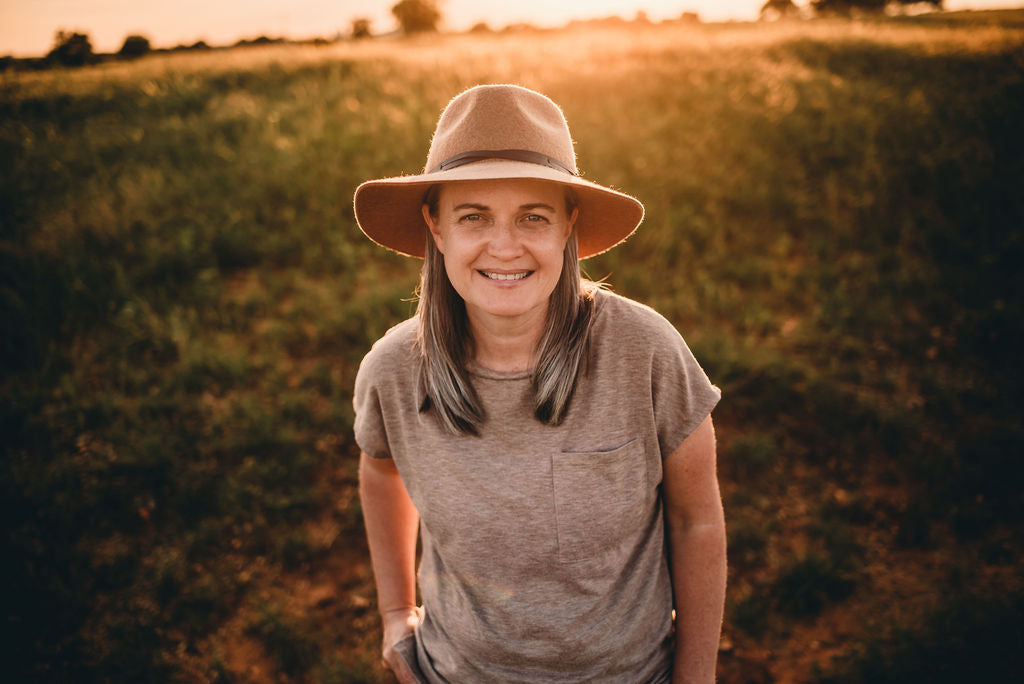 Smiling woman in a hat and t-shirt outdoors at sunset, calm nature background